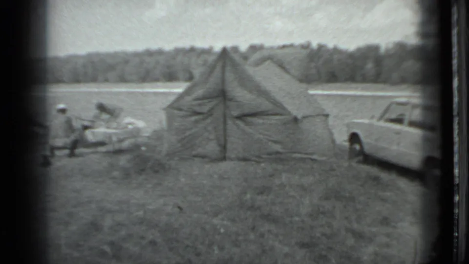 A few distant people appear near camping gear beside the tent, with part of the white station wagon at the frame edge.