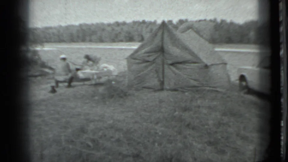 Distant figures remain near camp items beside the canvas tent, with the lake and forest visible behind them.