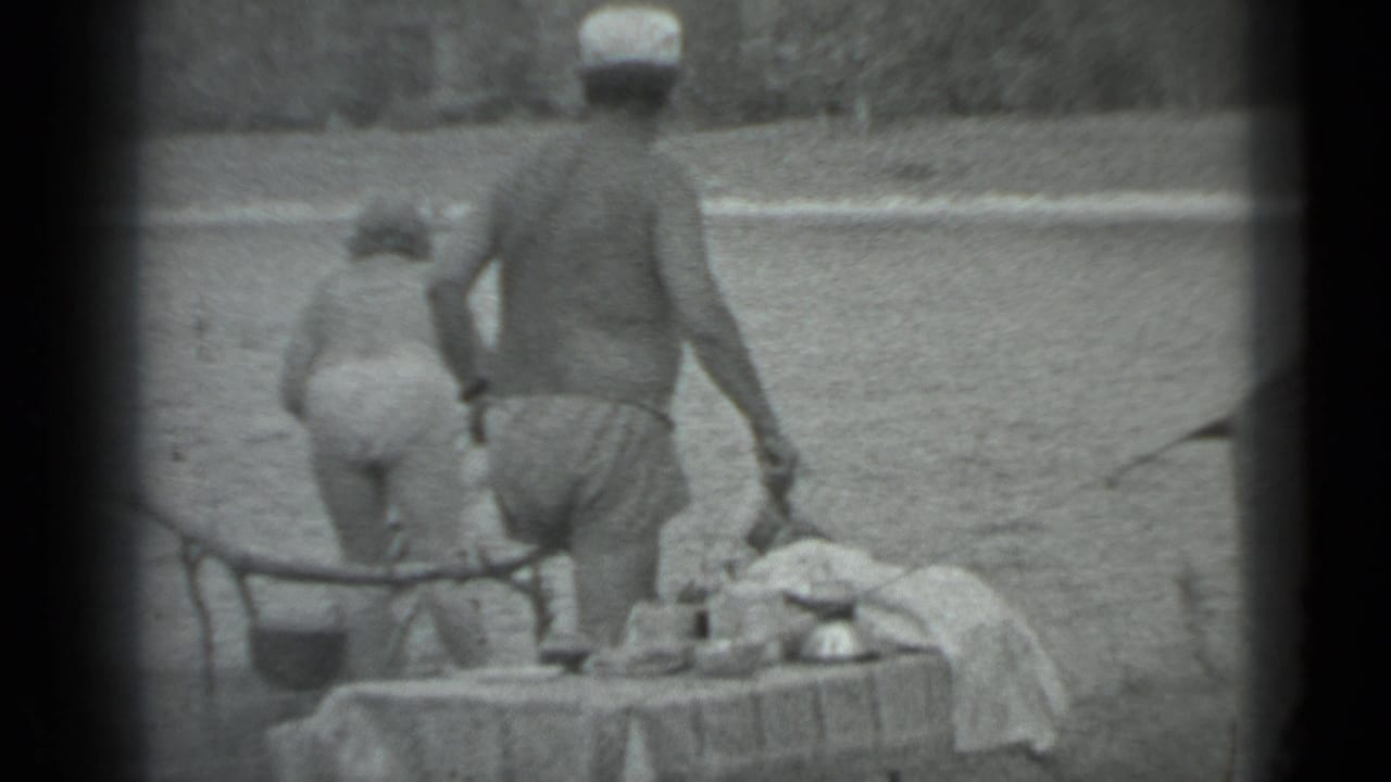 1983 Moscow lakeside camping frame with two people in swimwear near a table set with food or camp items.