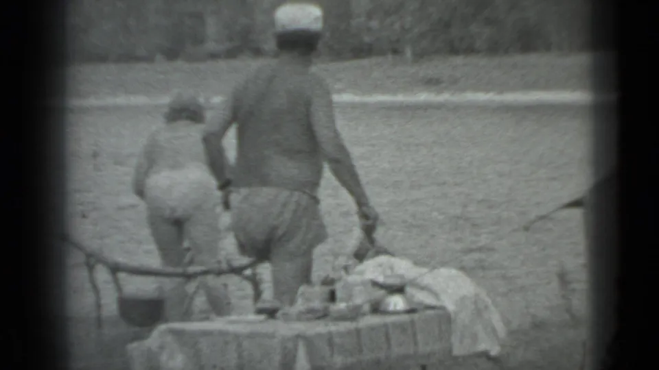 1983 Moscow lakeside camping frame with two people in swimwear near a table set with food or camp items.