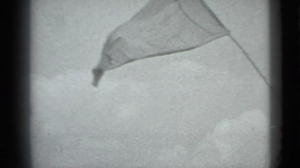 Soft black-and-white 8mm frame showing a flag or fabric panel extended against a bright background at the campground.