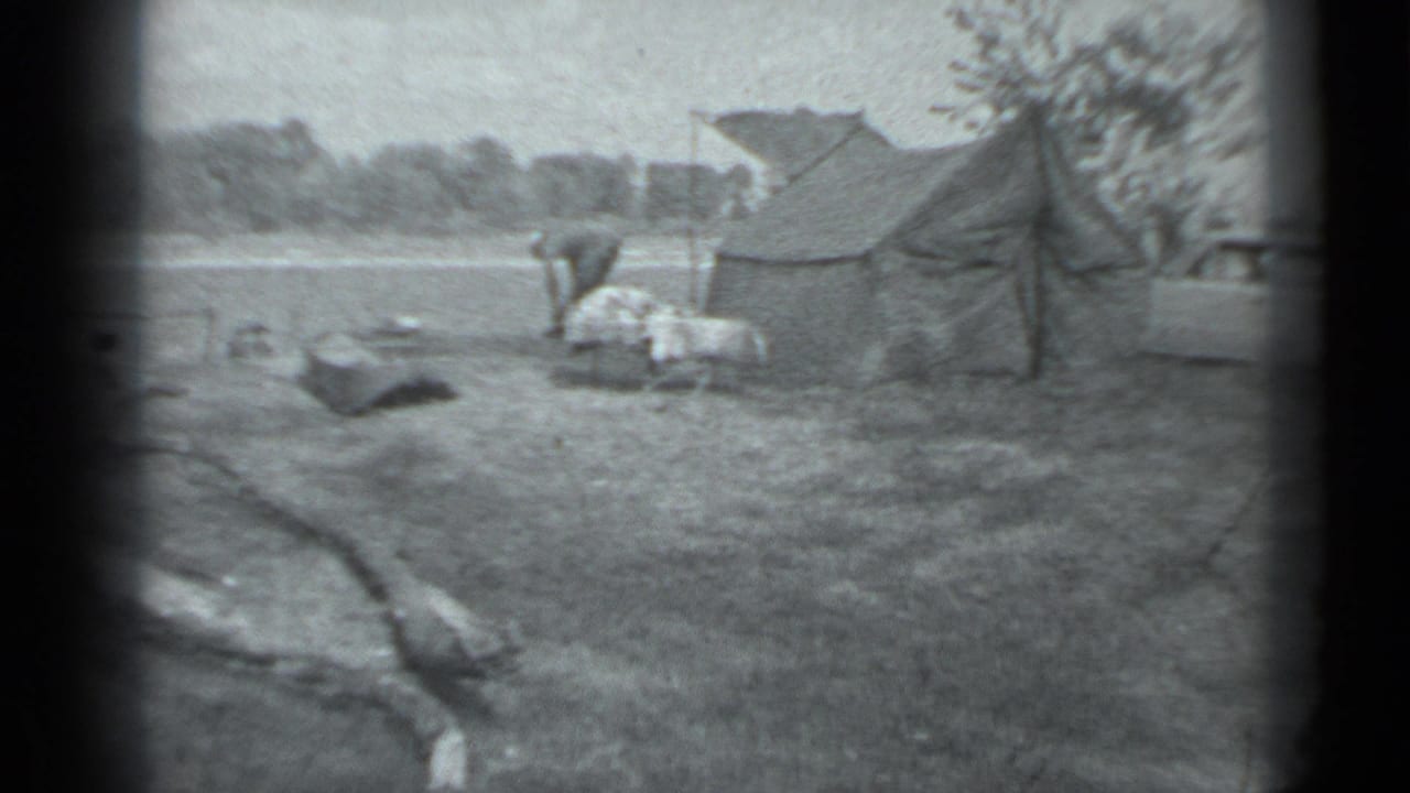 Grassy campsite with a canvas tent, station wagon, and a person bending near camp gear.