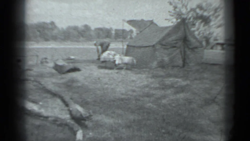 1983 Moscow home-movie frame showing a person working near a canvas tent with a light station wagon parked beside it.