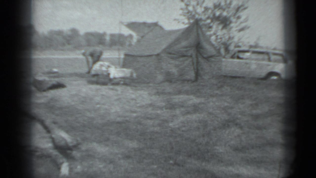 1983 Moscow campsite view with a canvas tent, a person by the gear, and a light-colored station wagon at frame right.