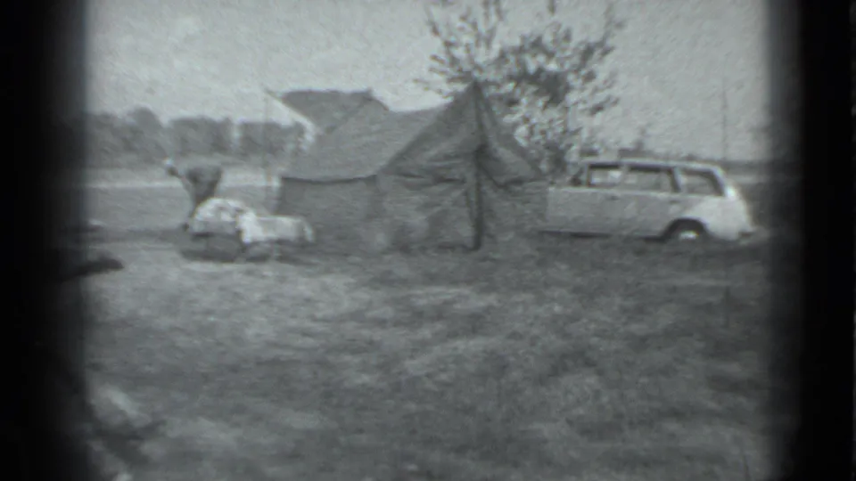 1983 Moscow home-movie frame of a person bending at a campsite beside a canvas tent and nearby station wagon.