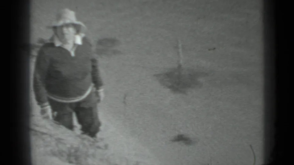 The hat-wearing figure appears closer to the camera while walking along the sandy lake edge in archival Moscow footage.