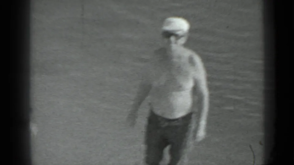 A shirtless person wearing a light cap appears near shallow lake water in the final frame of the 1983 Moscow home movie.