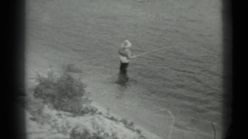 A distant view shows the woman standing in shallow water near the bank, with the fishing pole angled across the surface.