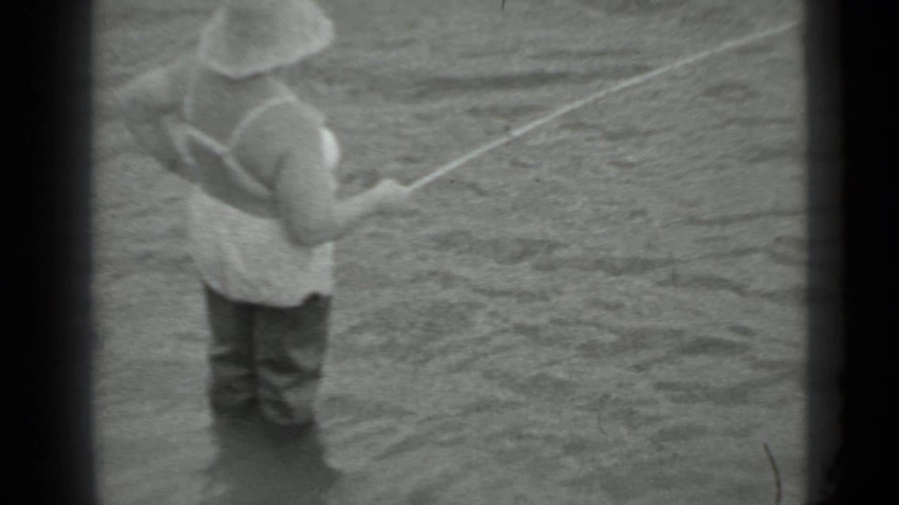Woman in a wide-brimmed hat stands in shallow water holding a fishing line.