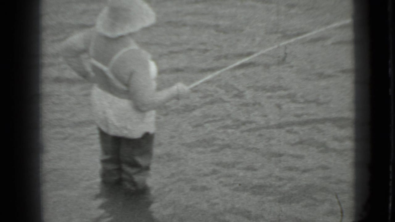 Black-and-white 8mm frame from Moscow in 1983 showing a woman fishing from shallow river water.