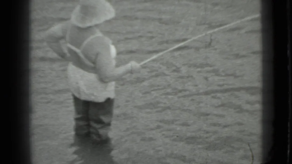Black-and-white 8mm frame from Moscow in 1983 showing a woman fishing from shallow river water.