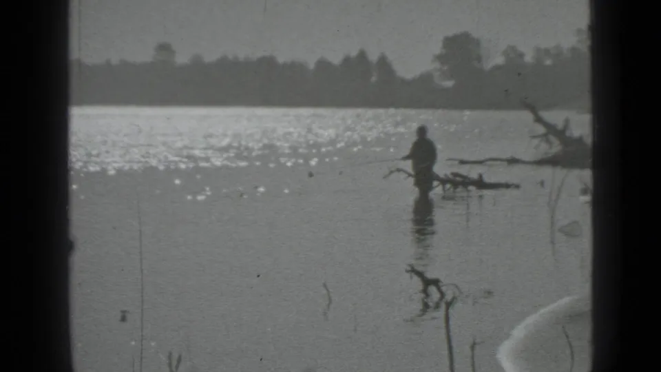 Distant 1983 Moscow lake view with a man fishing near branches while sunlight reflects across the water.