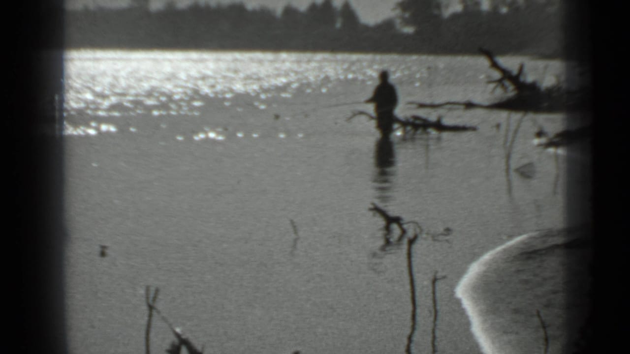 A distant man appears to fish while standing waist-deep in a calm Moscow-area lake in 1983 home-movie footage.
