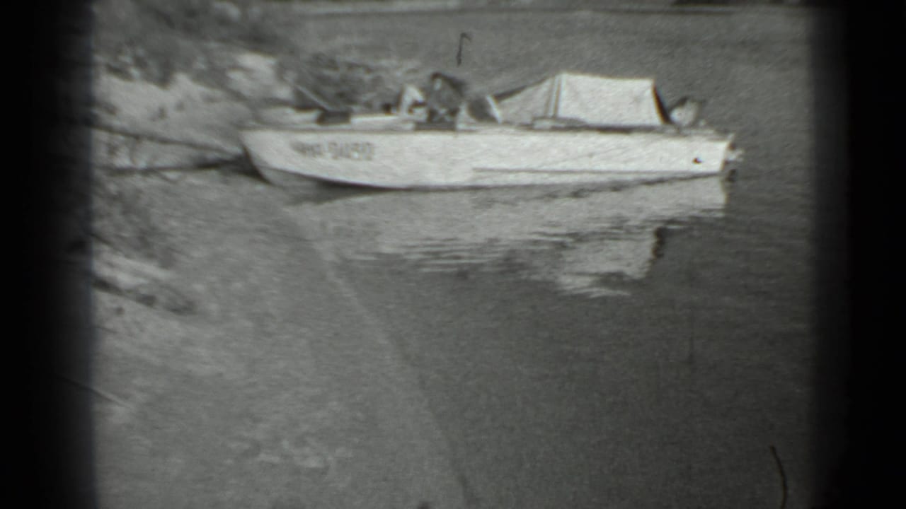 A small motorboat with a canvas cover sits close to the bank, its pale hull reflected in the water.