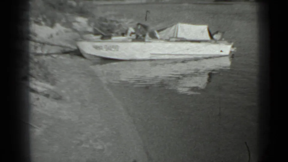 A small motorboat with a canvas cover sits close to the bank, its pale hull reflected in the water.