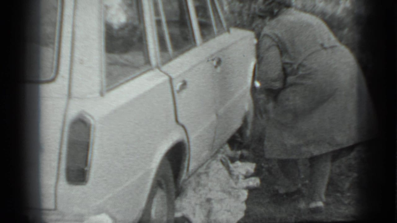 Woman bends beside a parked car with cloth on the ground.