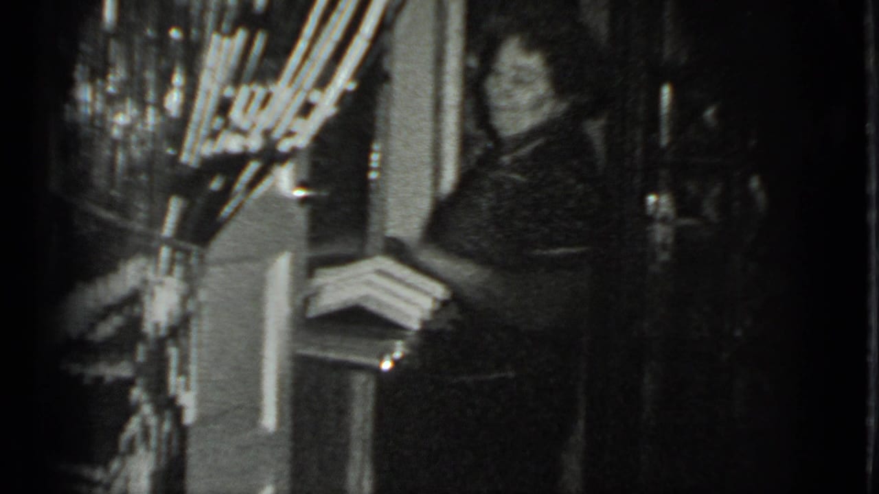 In a grainy 1983 Moscow home-movie frame, an adult woman stands in a doorway near shelves and household objects.