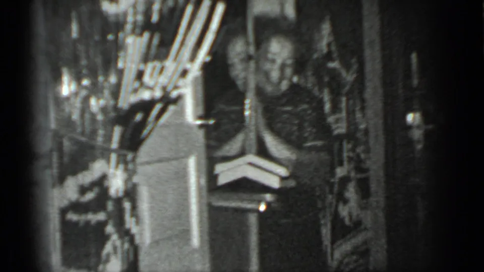 A black-and-white 8mm frame shows the woman near a doorway, partly surrounded by shelves and dark interior space.