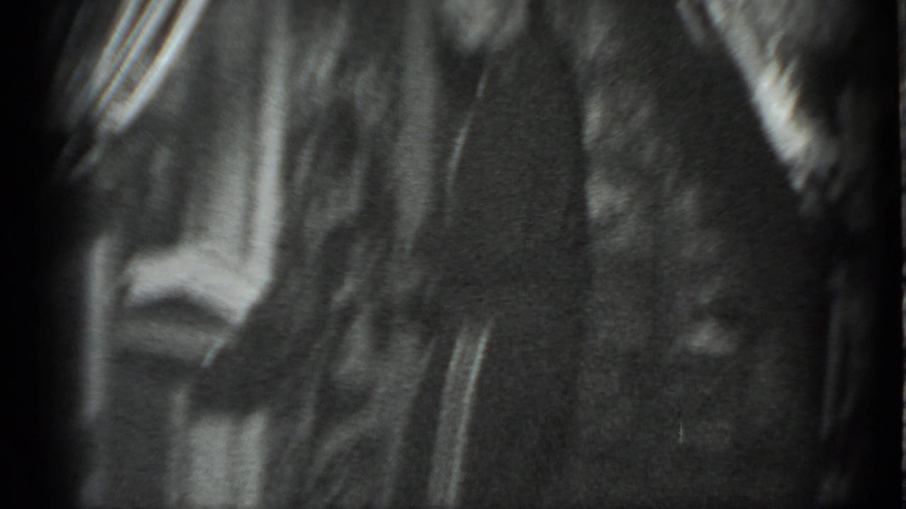 Grainy 1983 Moscow home-movie frame showing a dim interior doorway with a partially visible person passing nearby.