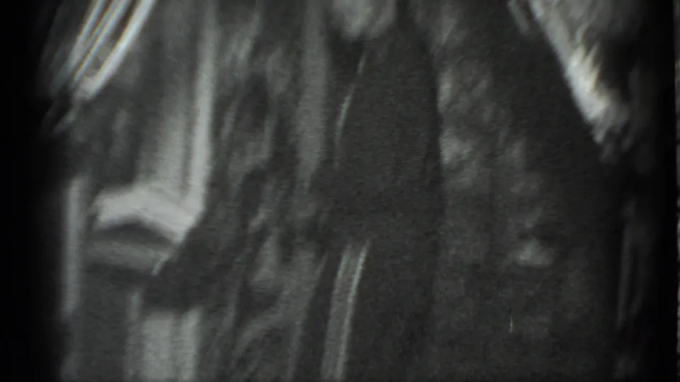 Grainy 1983 Moscow home-movie frame showing a dim interior doorway with a partially visible person passing nearby.