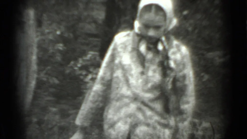 The woman in patterned outerwear bends near the bucket in a wooded Moscow setting, her headscarf and coat visible in soft focus.