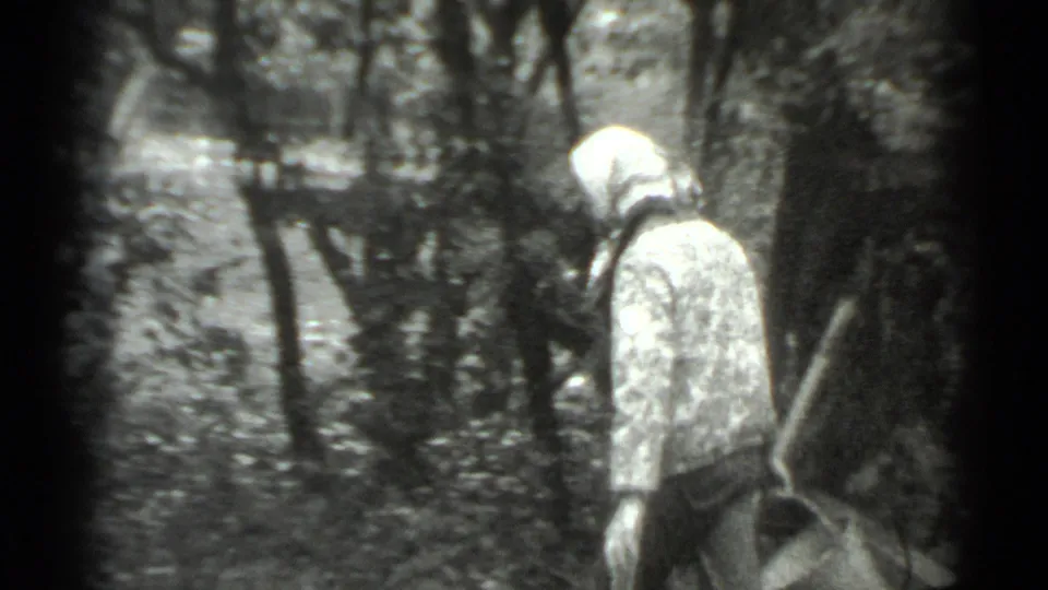 The woman in a headscarf stands near a tree and bucket in a wooded Moscow setting, seen through soft 8mm framing.