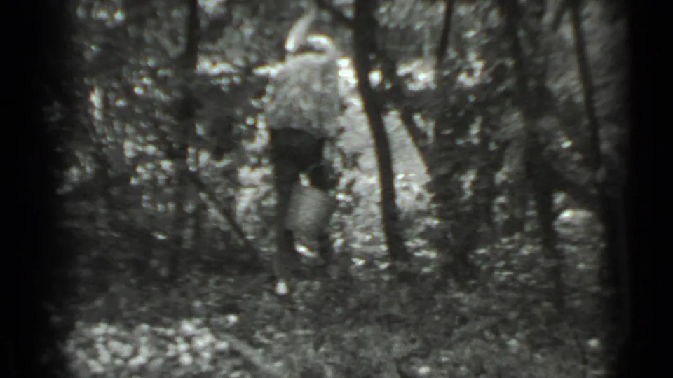In 1983 Moscow home-movie footage, a woman appears among trees carrying a bucket along a shaded path.