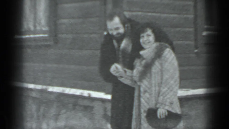 A smiling couple in winter clothing stands outside in the snowy Moscow setting, framed in soft black-and-white 8mm footage.