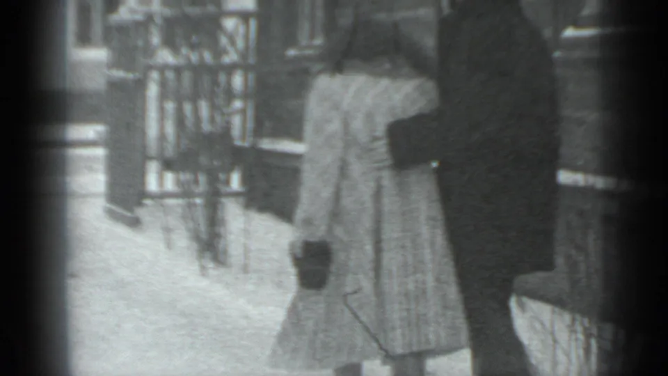 In Moscow 1983 home-movie footage, two bundled figures stand on snow beside a wooden building or fence.