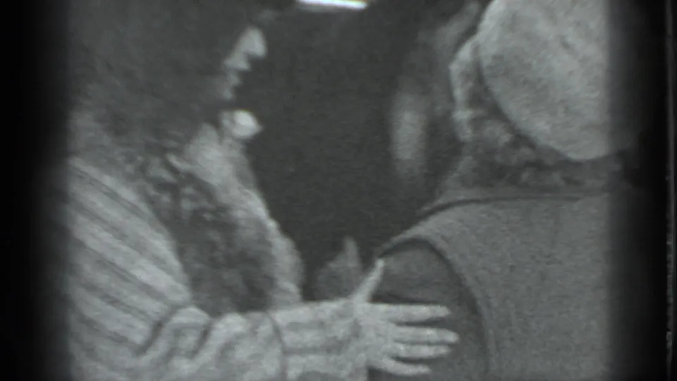 A woman in a light coat extends her hand toward a man in a fur hat during a snowy Moscow street greeting.