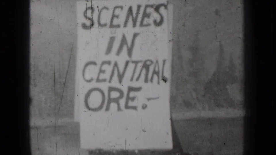 Close 1937 8mm view of a handmade Central Oregon sign, with grain, scratches, and soft outdoor background.