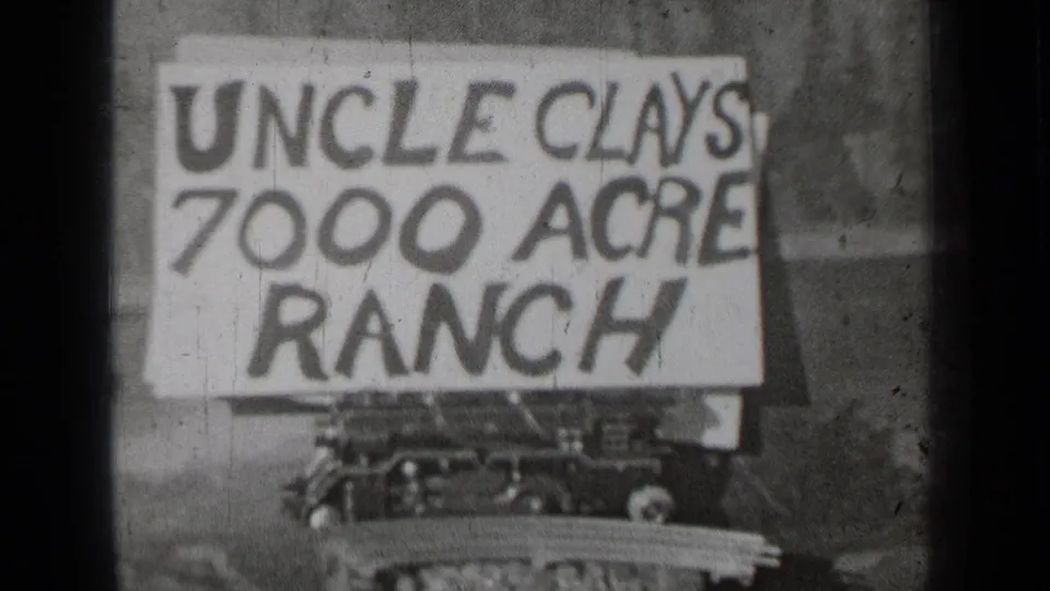Black-and-white 8mm frame from Bend, Oregon showing the same ranch advertisement sign mounted over a vehicle-like base.