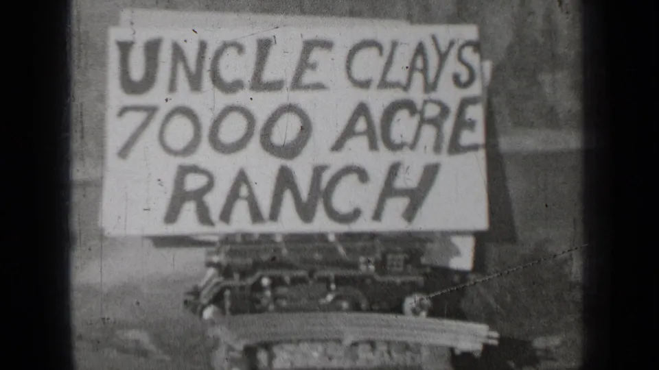 1937 home-movie frame of the Uncle Clays 7000 Acre Ranch sign, with grain, scratches, and a cropped base below.