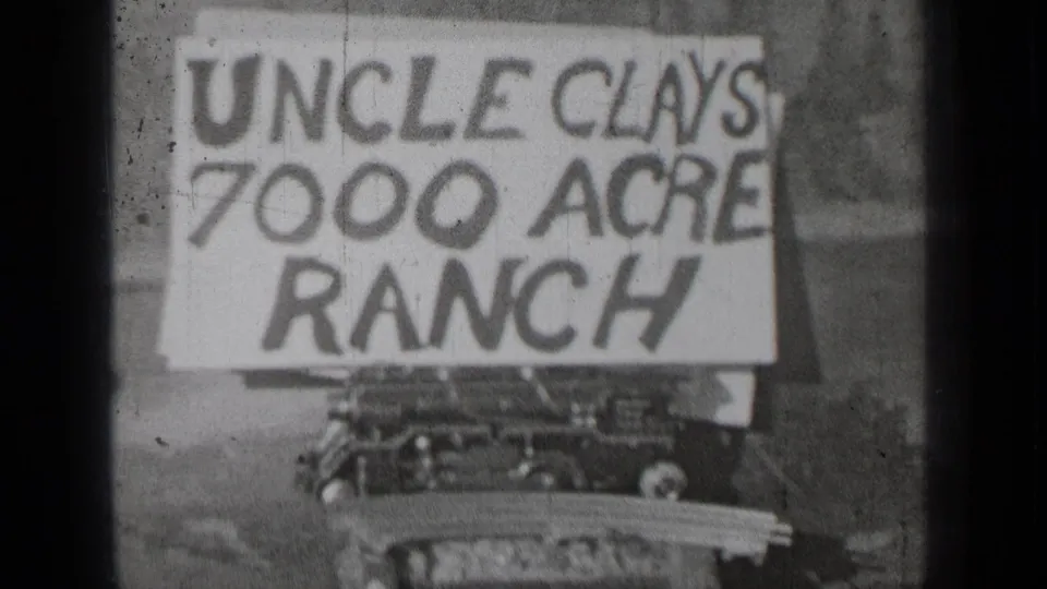 1937 Bend, Oregon home-movie frame showing a large hand-painted Uncle Clays 7000 Acre Ranch sign above a vehicle or machinery front.