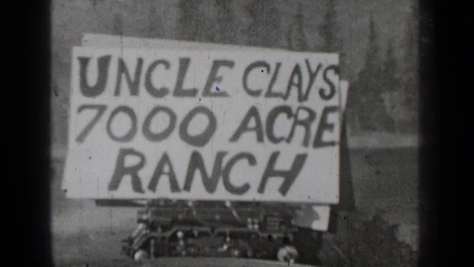 1937 Bend, Oregon home-movie frame with a large Uncle Clay’s 7000 Acre Ranch sign mounted near a car.