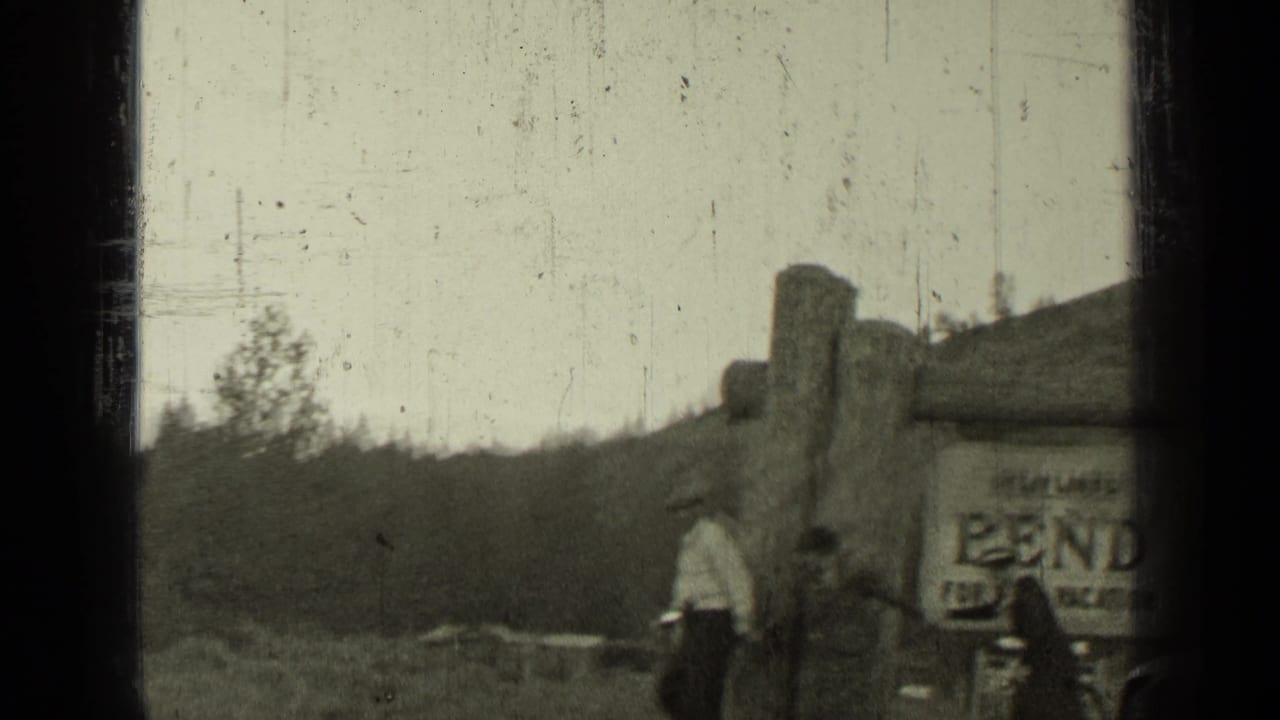 Visitors stand near a rustic building with a Bend sign and hills behind it.