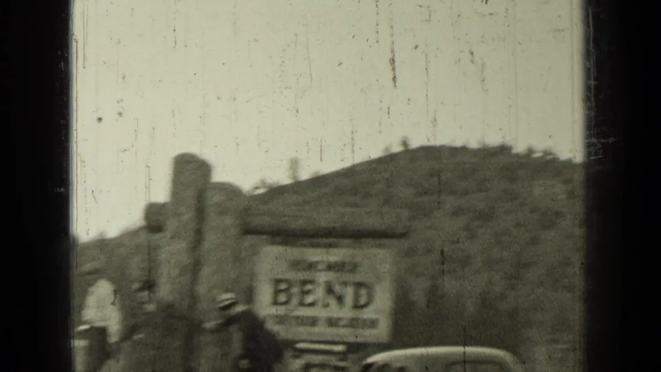 1937 Bend, Oregon home-movie view of a Bend sign on a rustic structure, with visitors and a partial car visible.