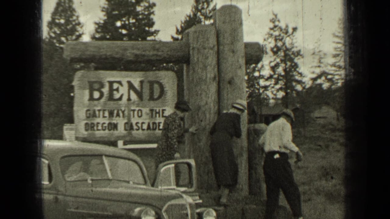 Travelers stand near a 1930s automobile at the Bend gateway to the Oregon Cascades sign.