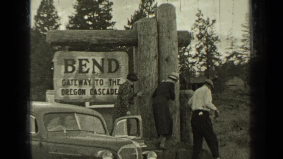 Travelers stand near a 1930s automobile at the Bend gateway to the Oregon Cascades sign.
