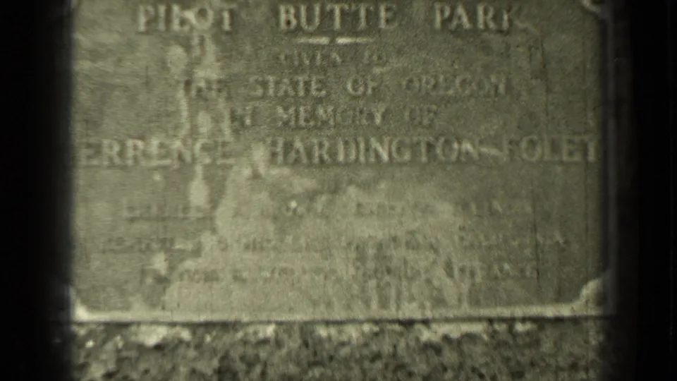 Final close 8mm frame of the Pilot Butte Park stone marker, with dark gate edges and faded dedication lettering visible.