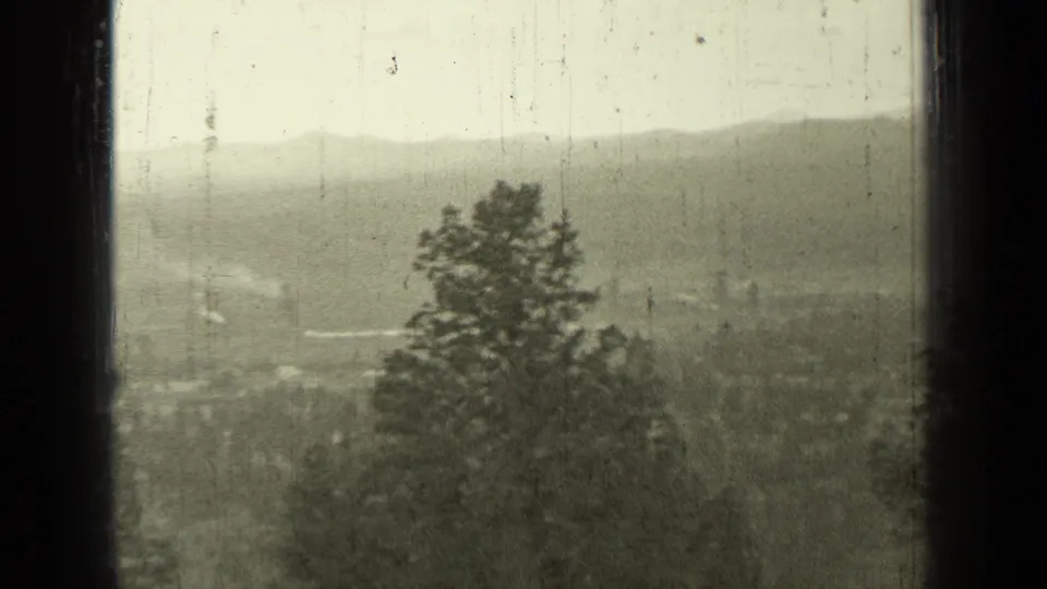 1937 Bend, Oregon hilltop view from Pilot Butte area with trees in the foreground, valley buildings, and distant mountains under haze.