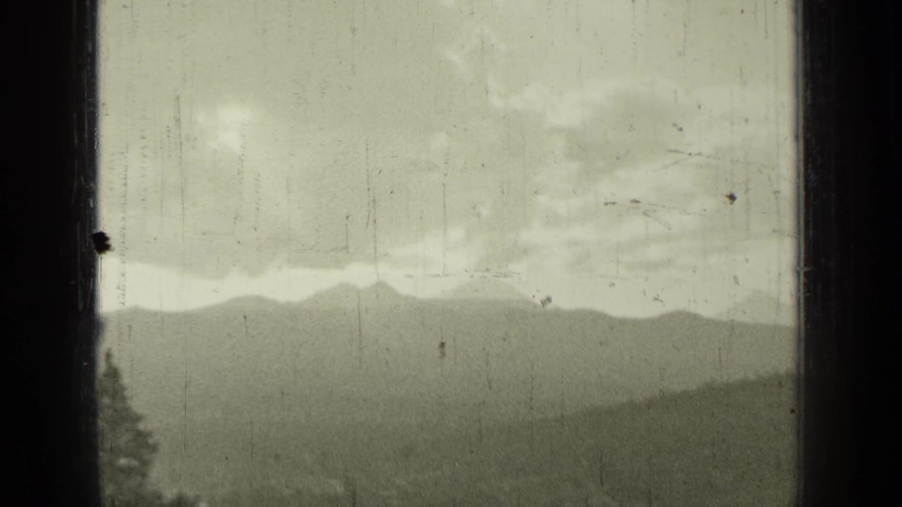 Distant mountain ridges and cloudy sky seen through a dark vertical window frame.