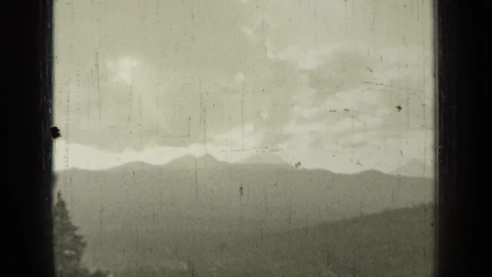 Window-framed 1937 Bend, Oregon view with layered hills, cloudy sky, soft focus, and visible 8mm film wear.