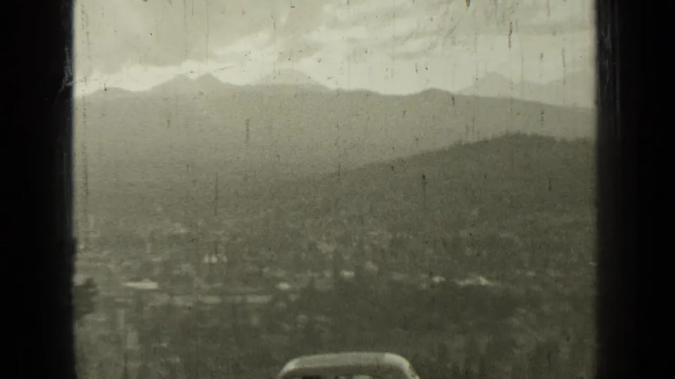 1937 Bend, Oregon panorama through a window, showing hills, town detail, and the front of a passing car at the lower edge.