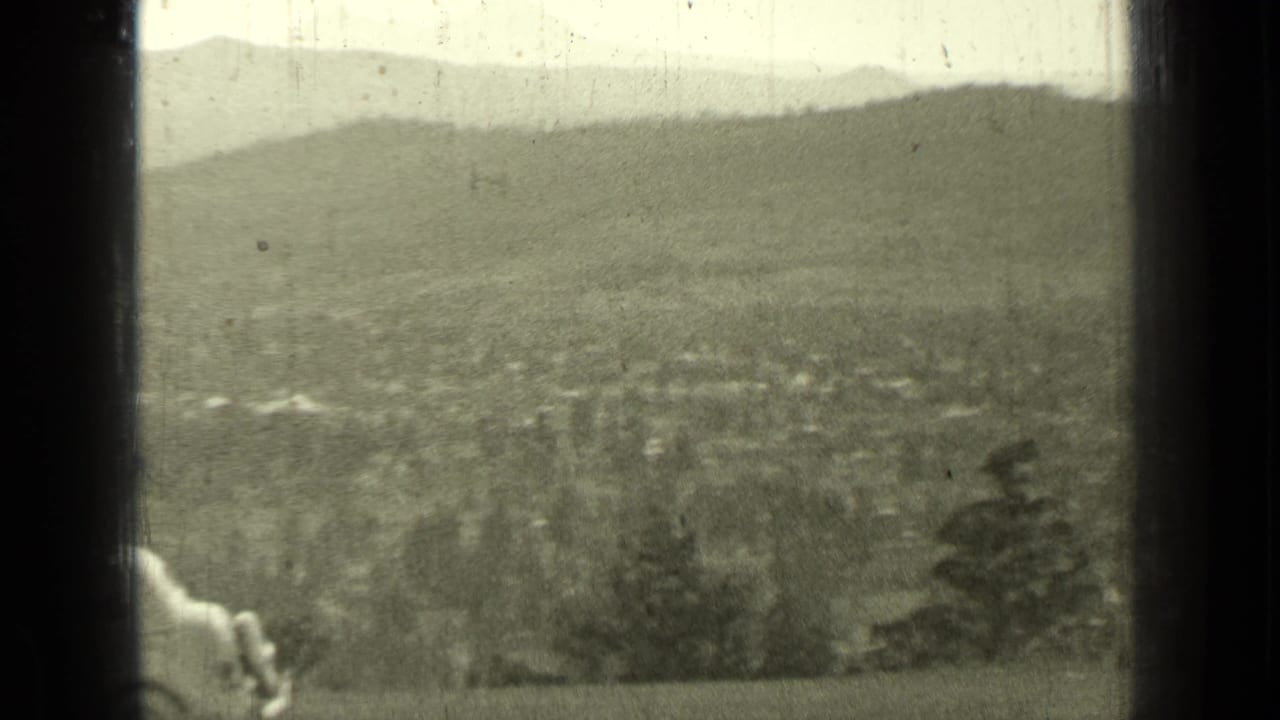 Distant valley and hills seen through dark film-frame edges with a partial figure or object at left.