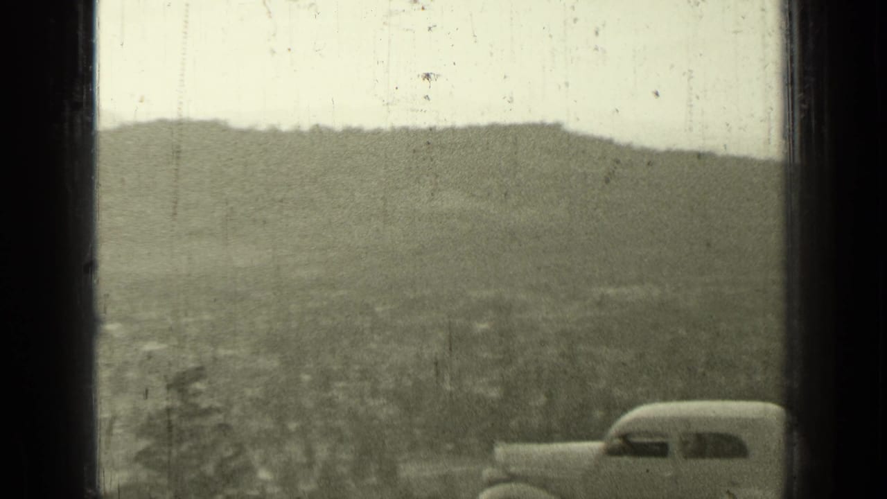 Vintage sedan partly visible at right with distant hills and valley in the background.