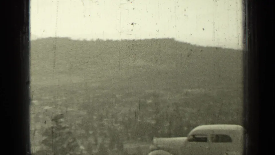 1937 Bend, Oregon frame with the rear portion of a rounded sedan at the right edge overlooking a broad valley and distant hills.