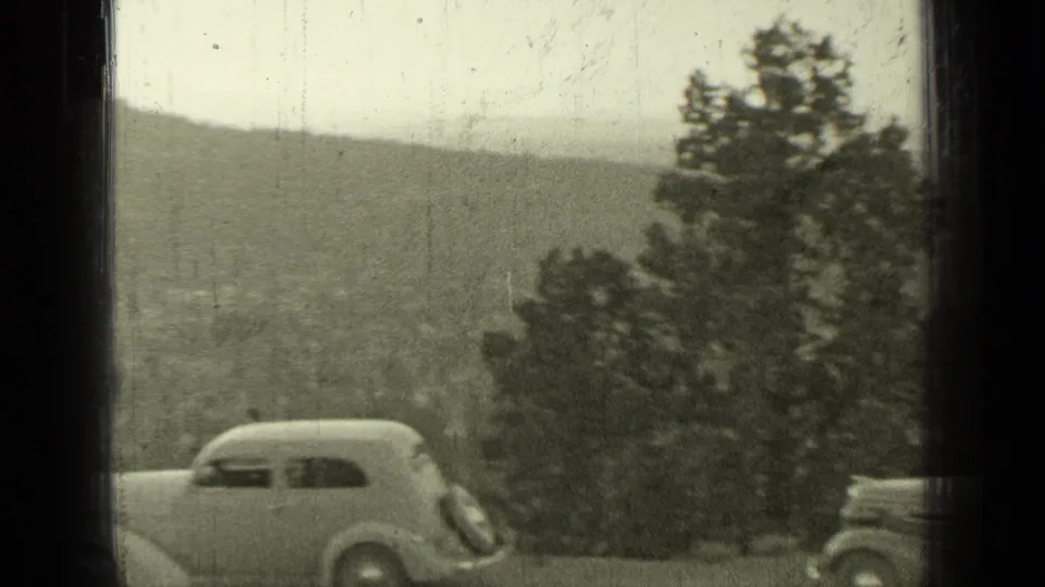 1937 Bend, Oregon frame showing a rounded sedan parked near pine trees on a hillside above the valley.