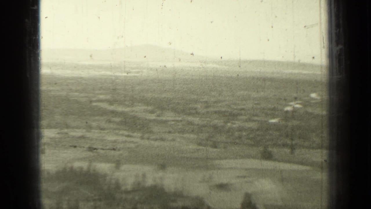Distant farmland and tree lines seen through dark vertical film borders under a pale cloudy sky.