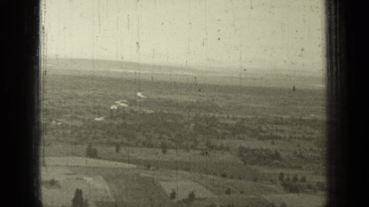 Soft distant view of fields, scattered trees, and pale sky framed by dark film edges.